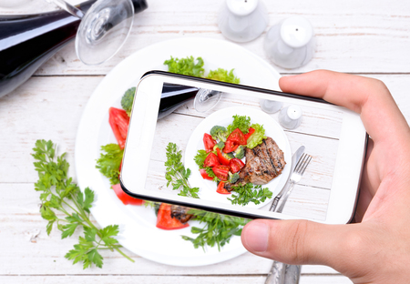 Hands taking photo grilled rib with grilled vegetables with smartphone.の写真素材