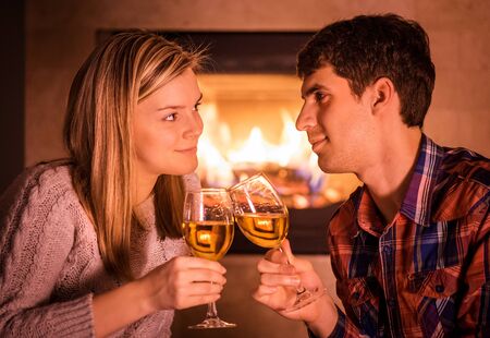 Happy young couple sitting near fireplace and drinking wineの写真素材