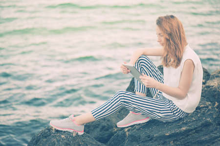Girl using a digital tablet by the sea.の写真素材