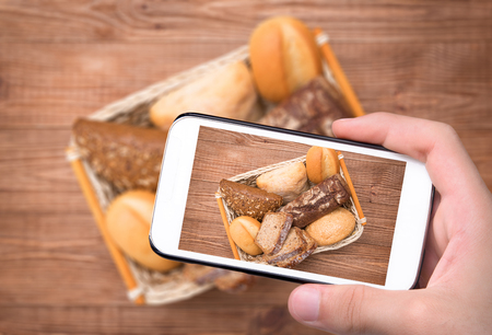 Hands taking photo baked bread with smartphone.