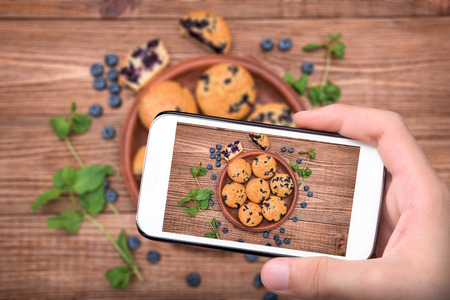 Hands taking photo blueberry muffins with smartphone.の写真素材