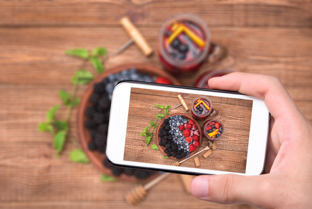 Hands taking photo red wine sangria with fresh berries with smartphone.の写真素材