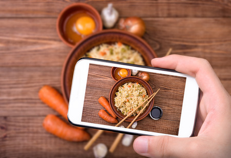 Hands taking photo fried rice with vegetables and eggs with smartphone.の写真素材