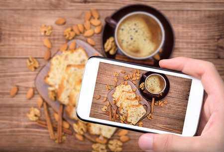 Hands taking photo nut cake with cup of coffe with smartphone.の写真素材