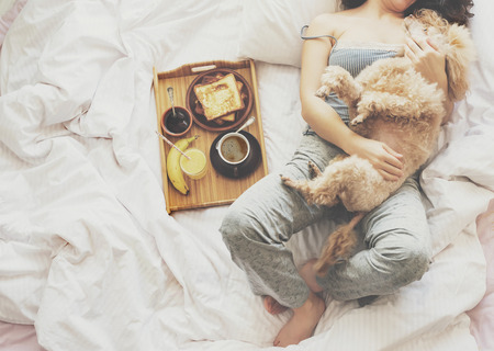 Young woman with her dog in a bed. Breakfast in bed - french toasts with a cup of coffee.の写真素材