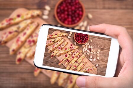 Hands taking photo biscotti with pistachios and cranberries with smartphone.の写真素材