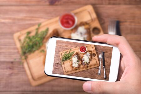 Hands taking photo baked chicken parmesan with smartphone.