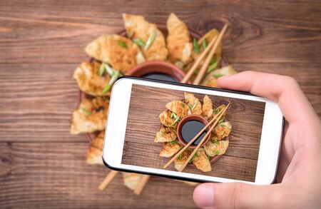 Hands taking photo homemade shicken potstickers with soy sauce with smartphone.