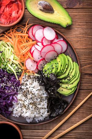 Sushi bowl with seaweed, avocado, radishes, cucumber, carrot red cabbage, and black sesame seeds.の写真素材