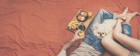 Young couple is lying in bed with dog and having a healthy breakfast.の写真素材