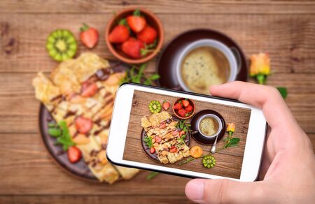 Hands taking photo of a pancakes with a berry and a cup of coffee with a smartphone.の写真素材