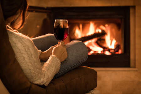 Young woman sitting at home by the fireplace and drinking a red wine.の写真素材