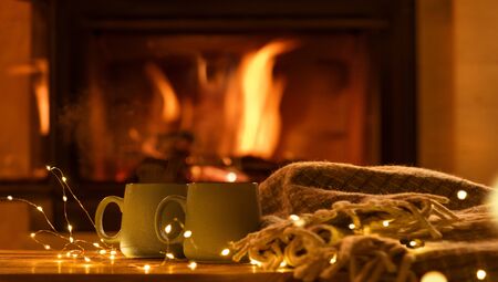 Steam from a cup with a hot cocoa on the fireplace background. Decoration garlands of lights.