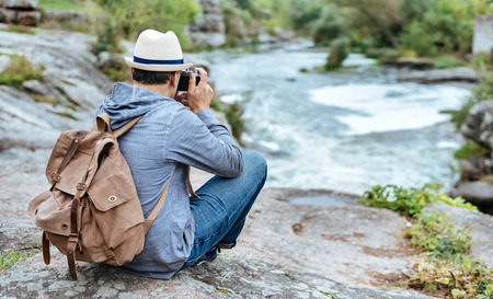 Man making pictures with a camera while traveling. Natural canyon with view of the mountain river....