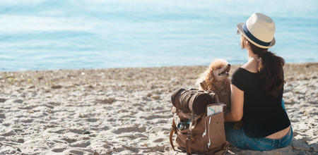 Woman traveler with backpack holding dog and looking at sea. Concept of travel.の写真素材