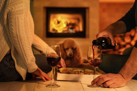 Young couple having romantic dinner with pizza and wine over fireplaceの写真素材