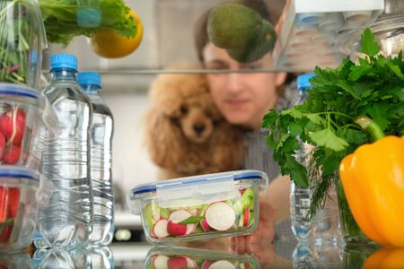 Woman looking inside a fridge full of food and choosing a salad in the container.の写真素材