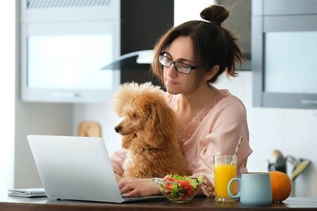 Young woman with her dog working using a laptop at home.の写真素材