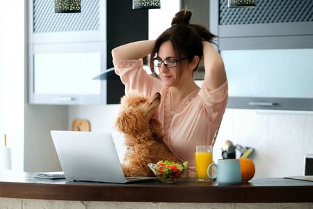 Young woman with her dog working using a laptop at home.の写真素材