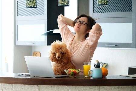 Young woman with her dog working using a laptop at home.の写真素材