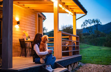 Woman with dog resting on the terrace mountain chalet at sunset.の写真素材