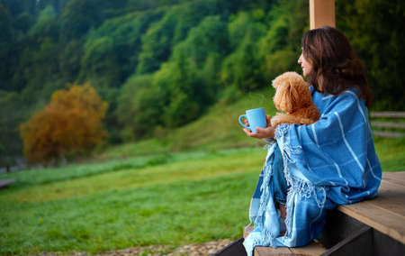 Woman with dog resting on the terrace mountain chalet at sunrise. Background with text space.の写真素材