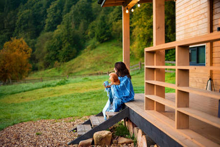 Woman with dog resting on the terrace mountain chalet at sunrise. Background with text space.の写真素材