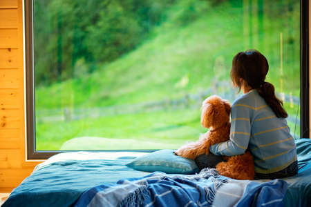 Woman sitting with her dog on the bed and looks outside the window seeing a mountain.の写真素材