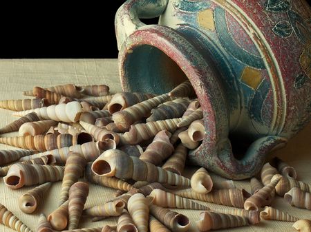 Hand painted clay pot dumping shells on textured cloth and black background