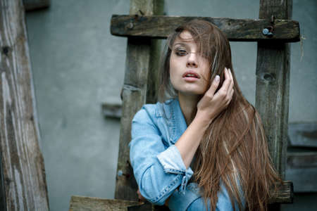young female wearing jean jacket outdoors adjusting her hair with handの写真素材