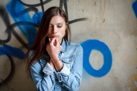 portrait of young female leaning against the wall  wearing a jean jacket with closed eyesの写真素材