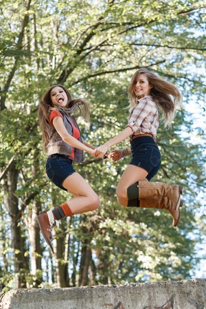 two young women jumping holding hands looking at cameraの写真素材