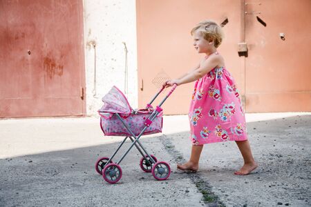 little girl walking barefoot with her carriage on cementの写真素材