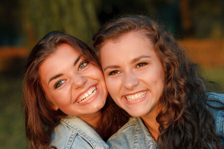 close-up portrait of two happy teenage girls outdoors in jeans wear smiling looking awayの写真素材