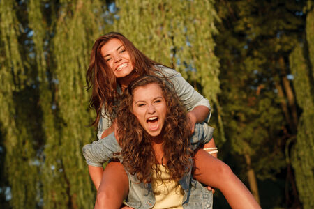 teenage girl giving her girlfriend piggyback ride in parkの写真素材