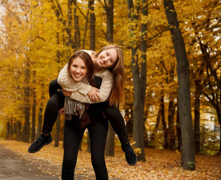 young female giving her friend piggyback ride in autumn forestの写真素材
