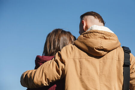 young male hugging female looking at her rear view blue sky on backgroundの写真素材