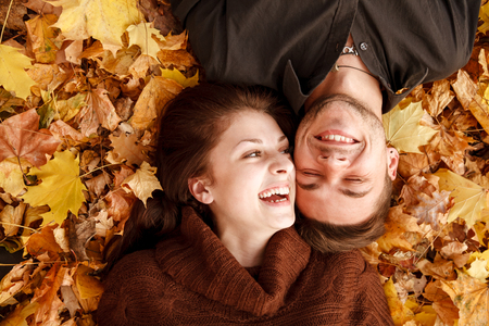 young couple lying down on autumn leaves laughing having good timeの写真素材