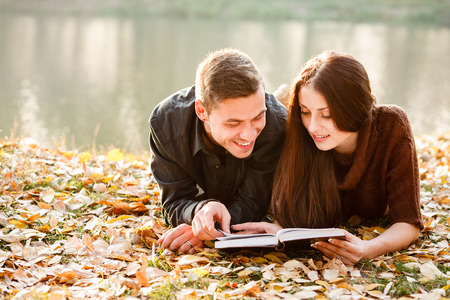 young male and female lying down near lake reading bookの写真素材