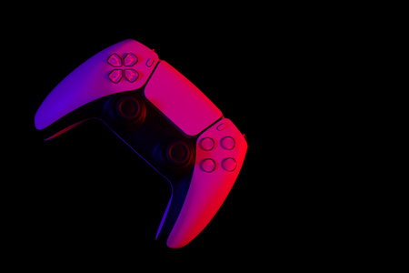 Modern white gamepad illuminated red and blue on a black background, top view.