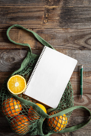 Mesh eco bag with oranges and blank notepad on wooden background, flat lay.の写真素材