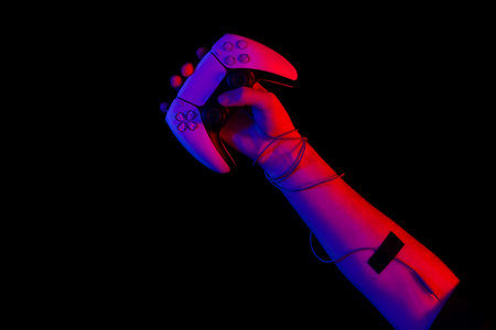 Male hand holding a gamepad in neon light on a black background, top view.