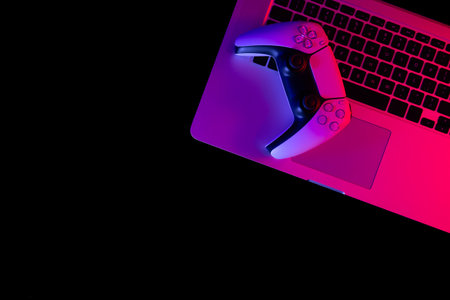 Gamepad and laptop with red and blue lights on a black background, top view.