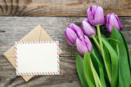 Purple tulip bouquet and blank greeting card on a wooden background, top view.の写真素材