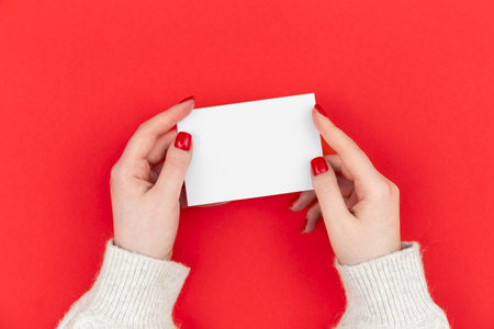 Empty paper in female hands on a red background, flat lay.の写真素材