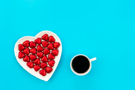 Heart shaped plate with heart shaped chocolates and coffee cup, flat lay.