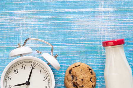 Alarm clock, cookie and a bottle of milk on a blue background, top view.の写真素材