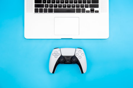 White gamepad and laptop on a blue background, flat lay.の写真素材