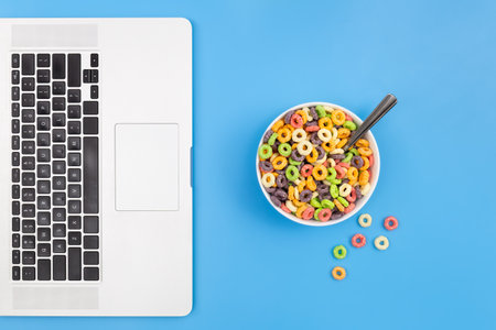 Colored breakfast cereal in a bowl and laptop on a blue background, flat lay.の写真素材