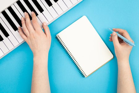 Female hands, blank notebook and piano on blue background, flat lay.の写真素材